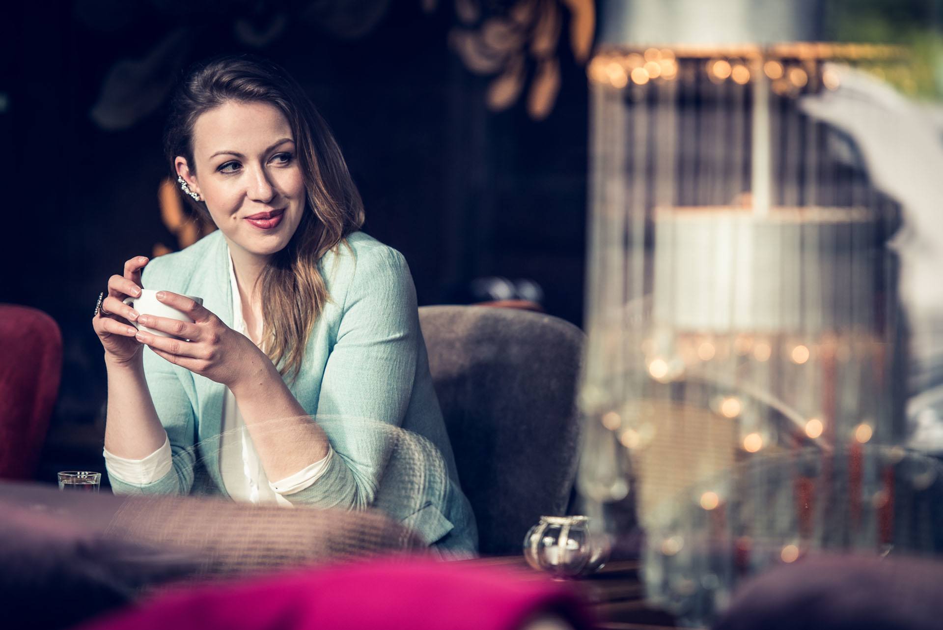 junge hübsche Frau sitzt mit Kaffeetasse hinter der Scheibe in einem Cafe und lächelt